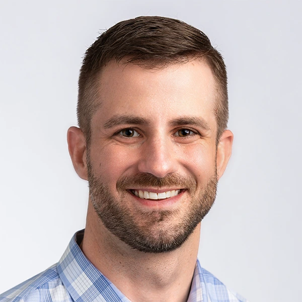 Headshot of Drew Madelung, smiling, in a light blue plaid shirt